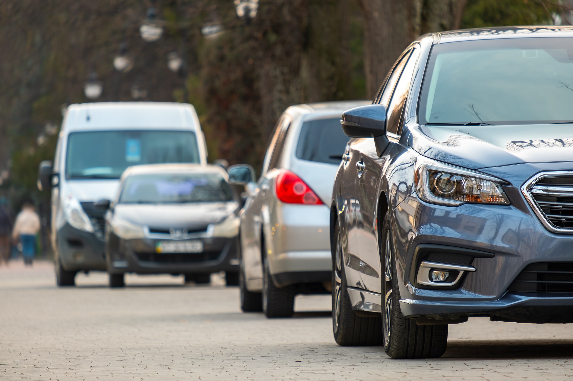 Cars parked in a row on a city street side on bright autumn day.